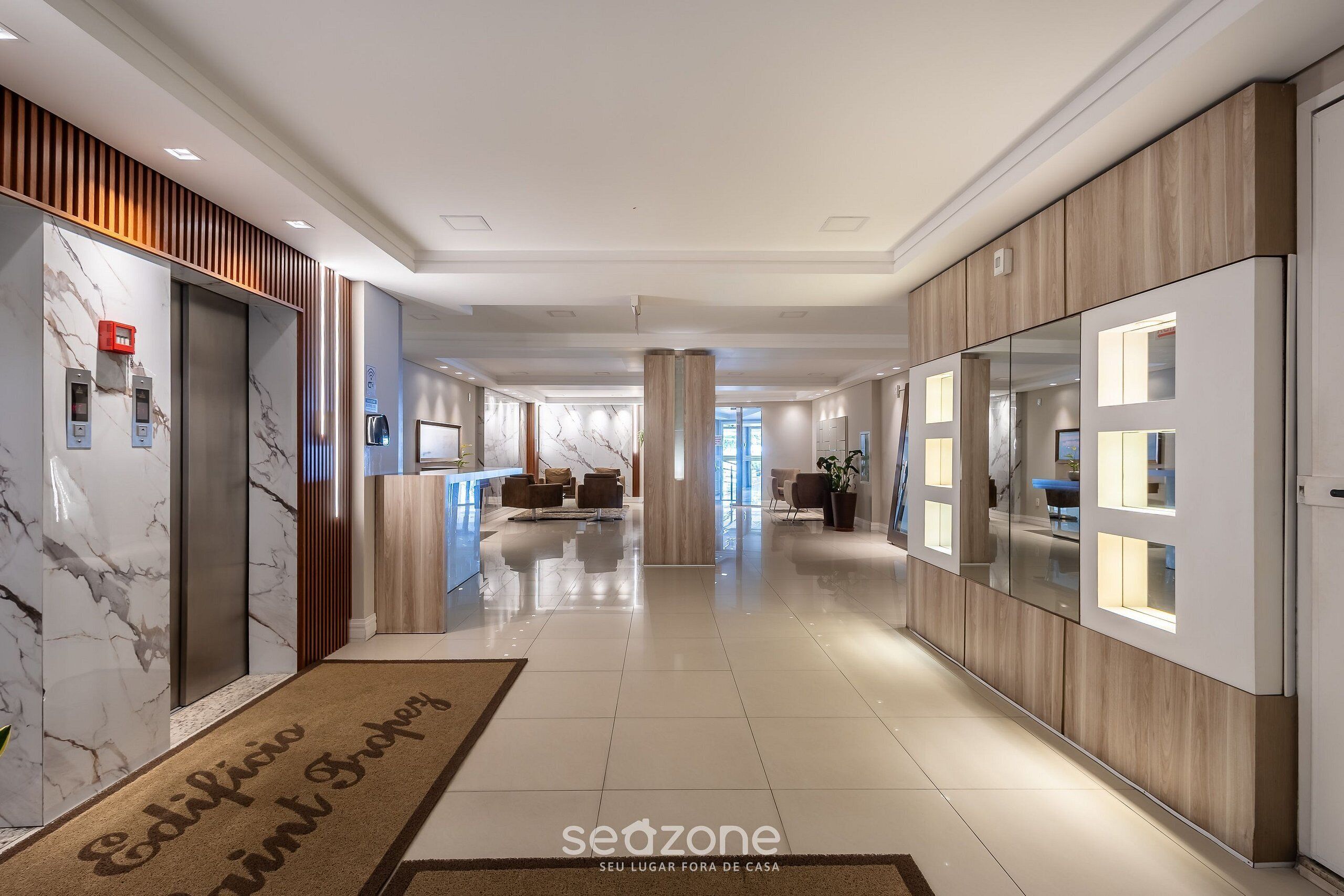 Un couloir d’hôtel aux murs de marbre, avec des boiseries, un comptoir de réception, un espace salon et une vue sur la chambre.