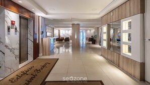 A modern hotel lobby with marble walls, wooden paneling, and a reception desk.