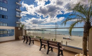 Un balcon donnant sur une plage, avec un palmier et un bâtiment en arrière-plan.