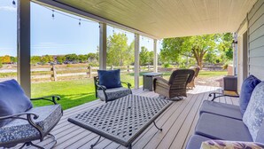 Un patio exterior techado con asientos, una mesa y vistas a un área cercada y árboles.
