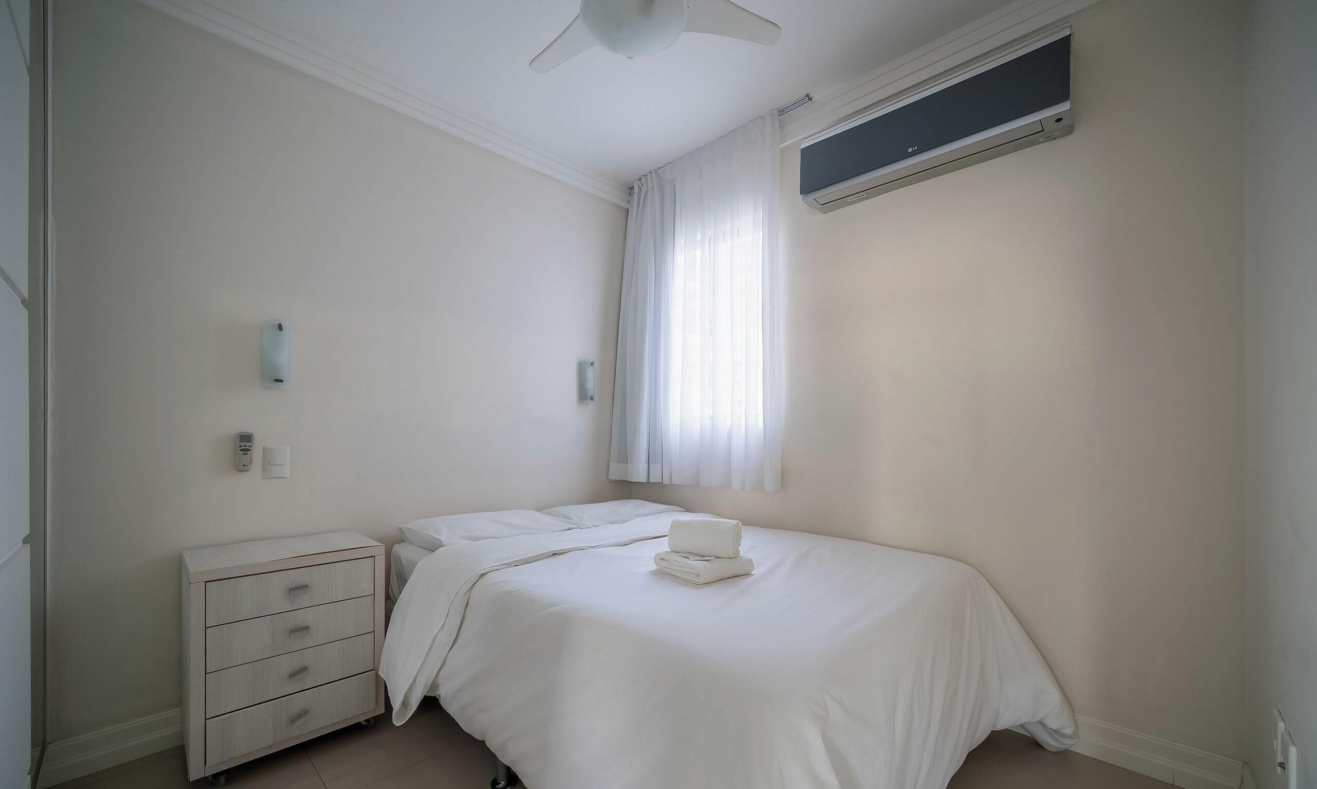Une chambre à coucher comprenant un lit, une table de chevet, une commode, un ventilateur de plafond et un appareil de climatisation.