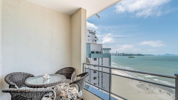 Balcón con sillas de mimbre y una mesa de vidrio con vista a la playa y al paisaje urbano.