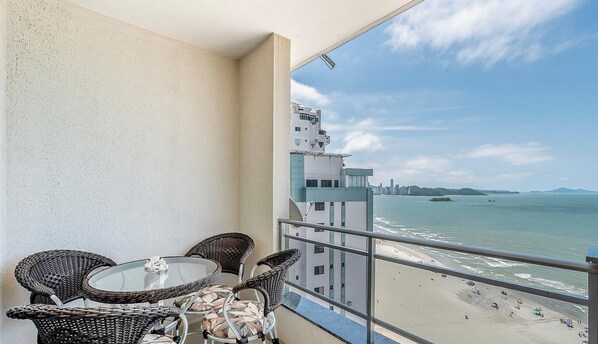 A balcony with wicker chairs and a glass table overlooking a beach and cityscape. - Cozy 3BR apt W/balcony sea View Cet1702 (Balneário Camboriú)