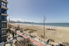 A beach with a city skyline in the background, a clear sky, and a few tents on the sand. - Cozy 3BR apt W/balcony sea View Cet1702 (Balneário Camboriú)