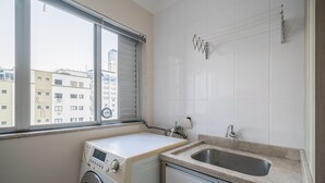 Zona de lavandería con lavadora, lavabo y ventana con vistas a edificios.