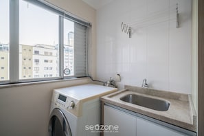 A laundry area with a washing machine, a sink, and a window with a view of buildings.