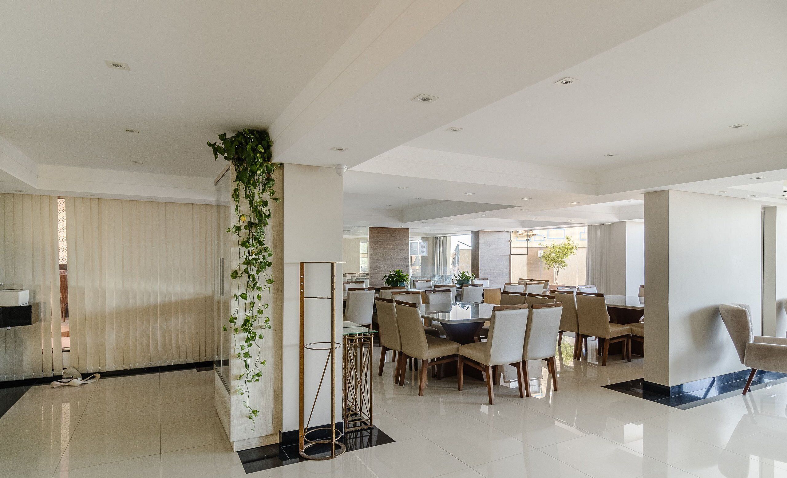 A modern dining area with a high ceiling, recessed lighting, and a central column with greenery.