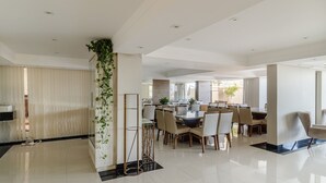 Un área de comedor moderna con techo alto, iluminación empotrada y una columna central con plantas.