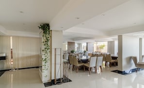 A modern dining area with a high ceiling, recessed lighting, and a central column with greenery.