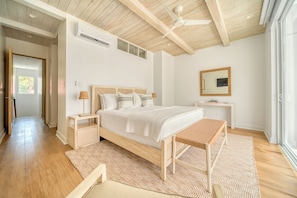 Un dormitorio con cama, mesitas de noche, un banco, un ventilador de techo y un ventanal grande.