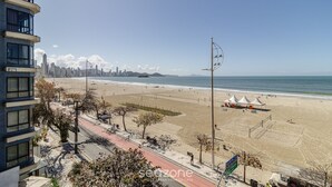 A beach with a city skyline in the background, a clear sky, and a few tents on the sand.