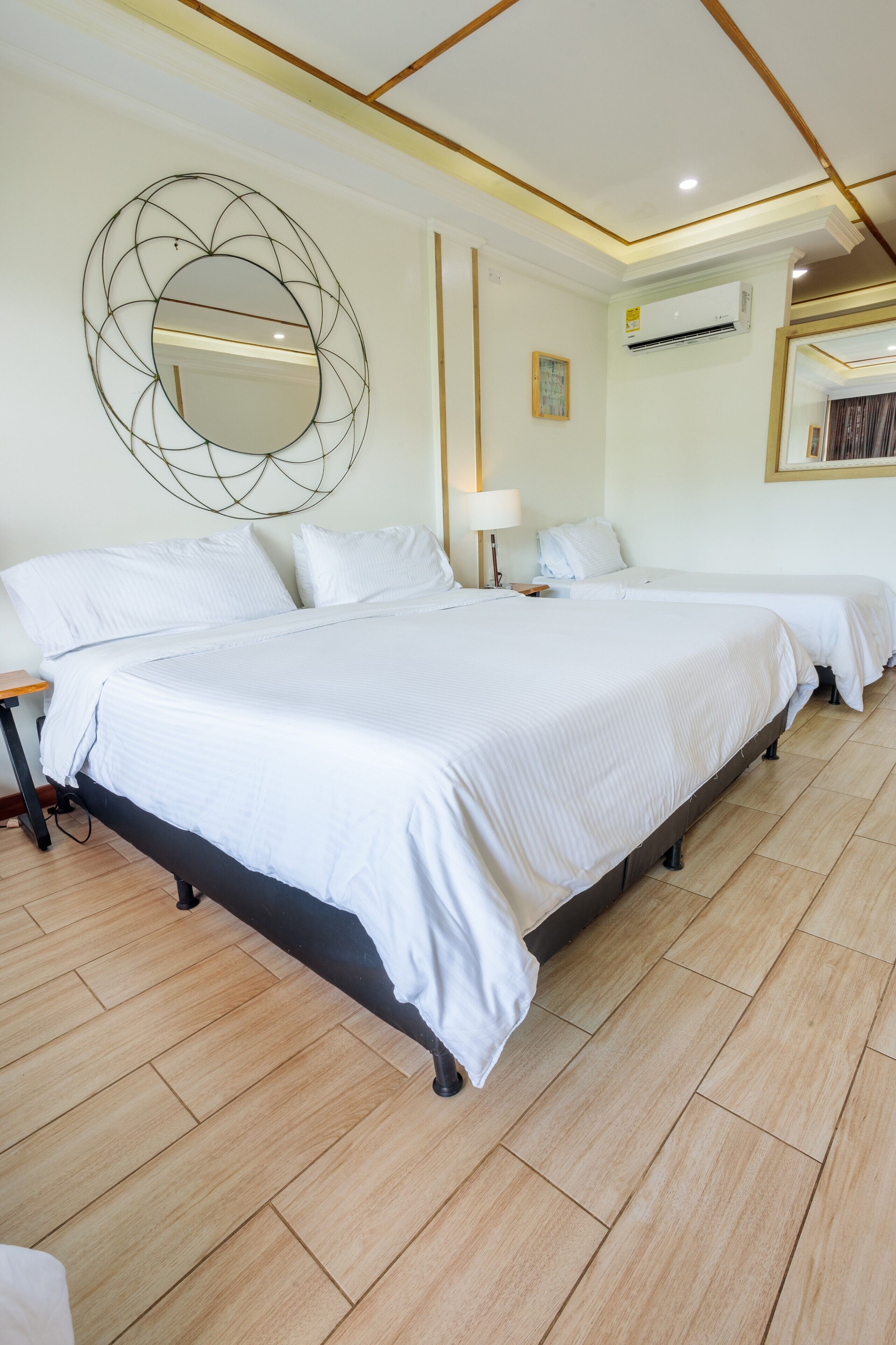 Ein Hotelzimmer mit einem großen Bett, zwei Nachttischen, einem Wandspiegel und einer Klimaanlage.