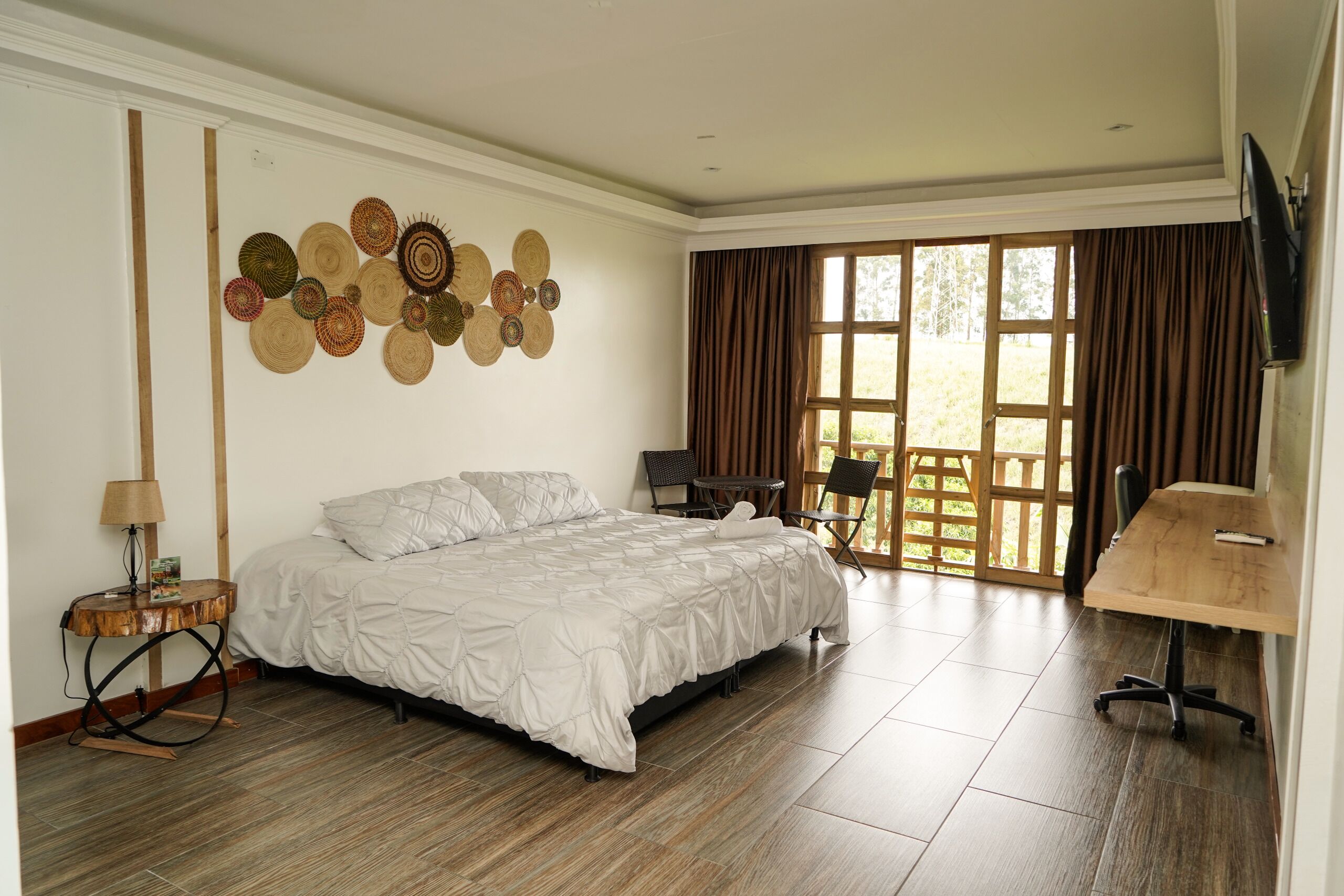 A bedroom with a bed, a desk, a chair, a lamp, and a wall with woven baskets.