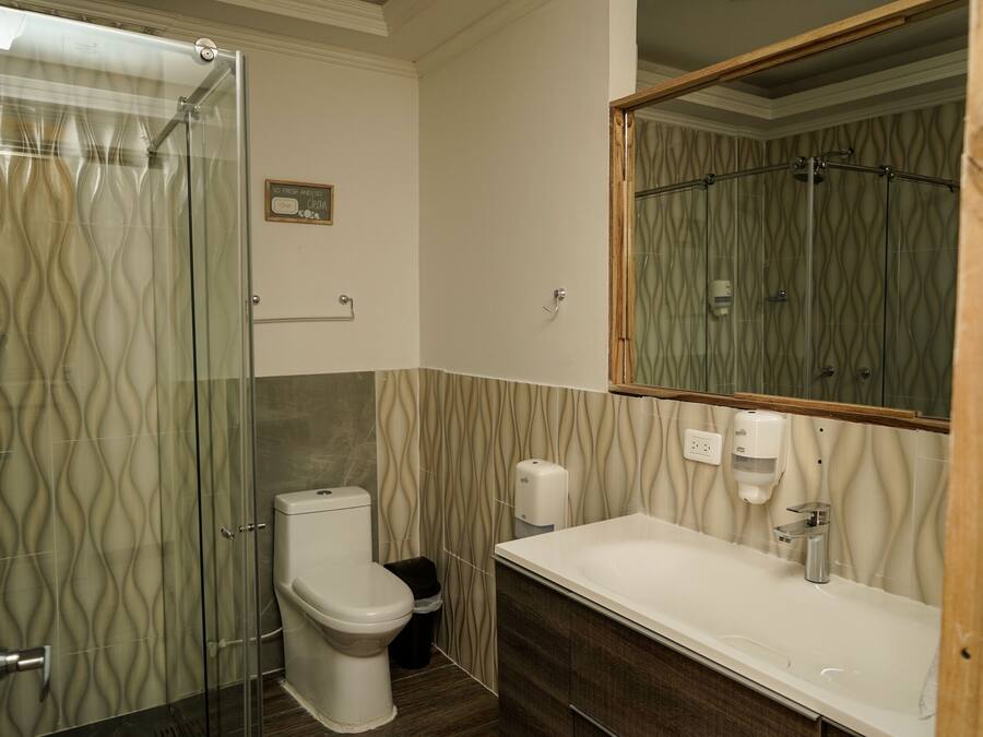 Un baño con cabina de ducha de vidrio, inodoro, lavamanos con dispensador de jabón y espejo.