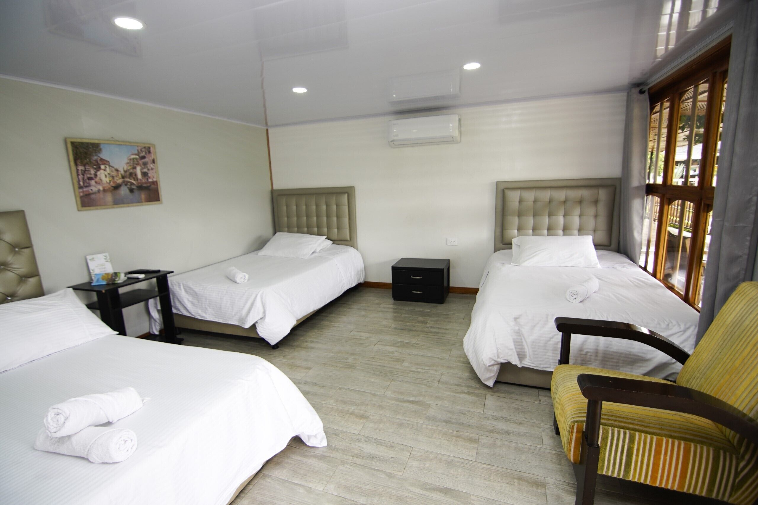 Une chambre d’hôtel avec trois lits, une chaise, une table de chevet et un appareil de climatisation.