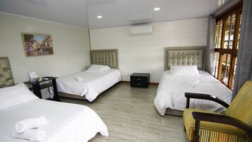 Une chambre d’hôtel avec trois lits, une chaise, une table de chevet et un appareil de climatisation.