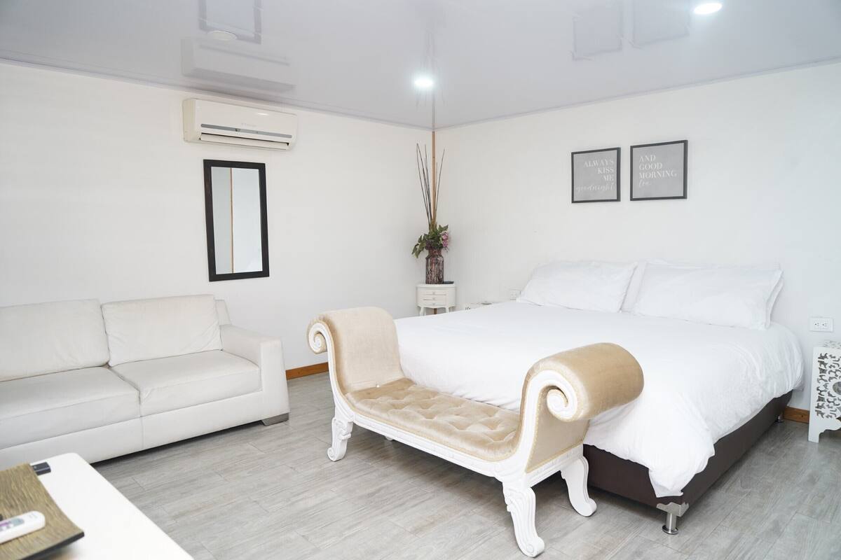 Un dormitorio con una cama, un sofá blanco, una mesita y un jarrón decorativo.