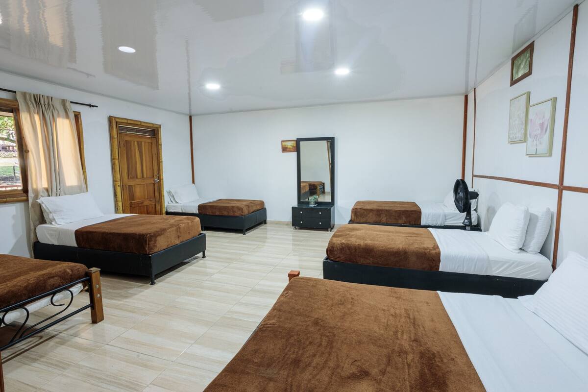 Habitación de hotel con cuatro camas, una puerta de madera, un espejo y un aparador.