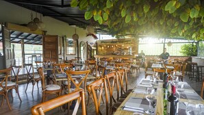 A restaurant with wooden chairs and tables, a bar area, and hanging plants.