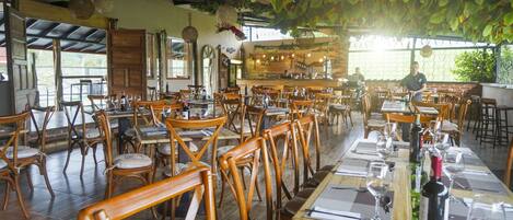 Ein Restaurant mit Holztischen und -stühlen, einer Bar und hängenden Pflanzen.