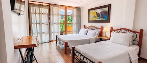 A hotel room with two beds, a wooden desk, and a large window with curtains.