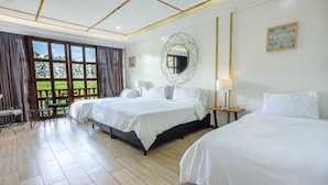 A hotel room with two beds, a large window with curtains, a dining table, and a view of greenery outside.