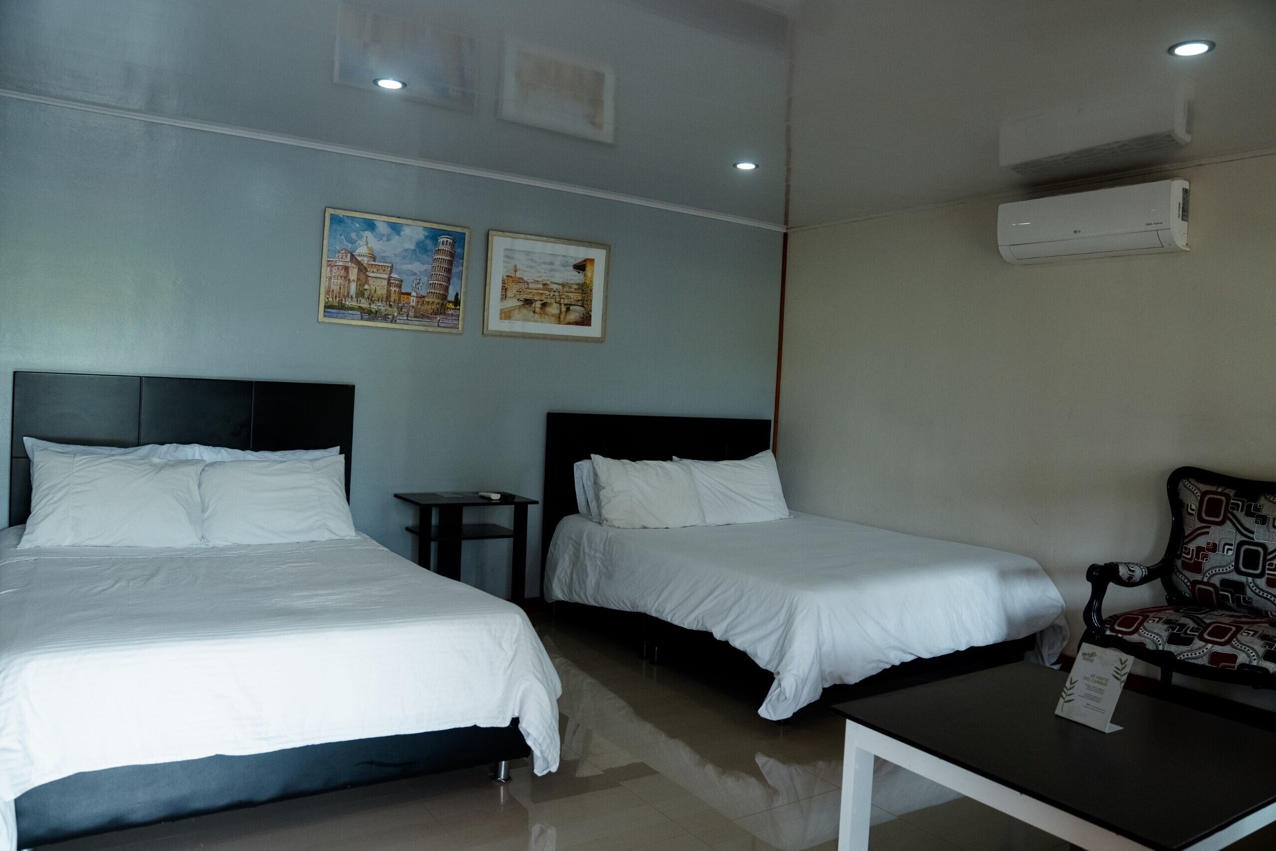 Een hotelkamer met twee bedden, een klein tafeltje, een stoel en een airconditioning.