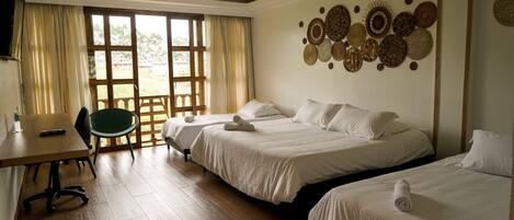 Habitación de hotel con dos camas, un escritorio y una silla. Se aprecia un ventanal con cortinas, y una pared decorada con cestas tejidas.