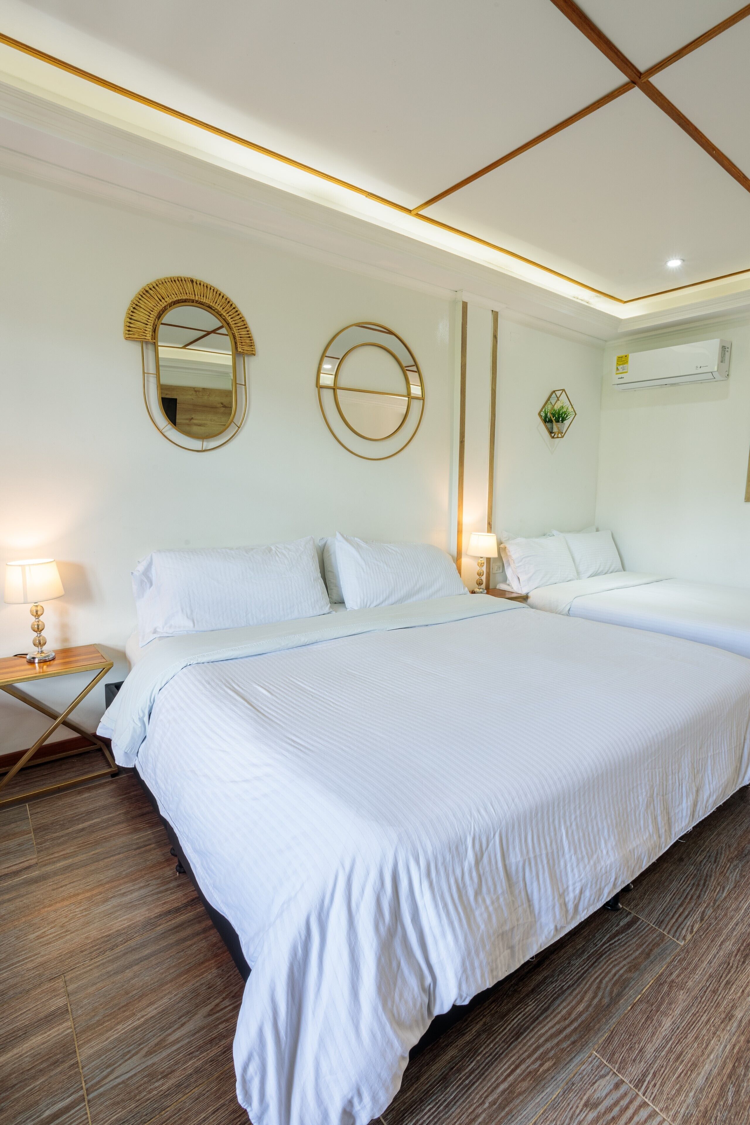 A large bed with white linens, a wooden floor, and a wall-mounted mirror.
