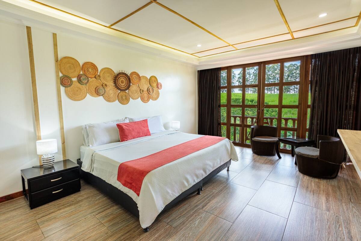Habitación de hotel con una cama grande, una mesita de noche, una silla y vista a un jardín a través de una ventana.