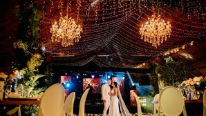 A wedding reception with a decorated stage, chandeliers, and floral arrangements.