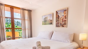 A hotel room with a large bed, wooden flooring, a window with curtains, and two wall-mounted paintings.