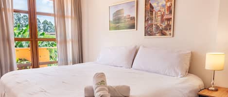 Habitación de hotel con una cama grande, piso de madera, una ventana con cortinas y dos cuadros colgados en la pared.