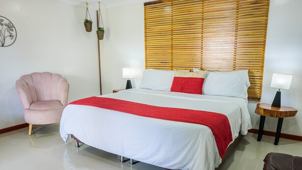 A hotel room with a bed, a chair, a bedside table with a lamp, and a wooden headboard.