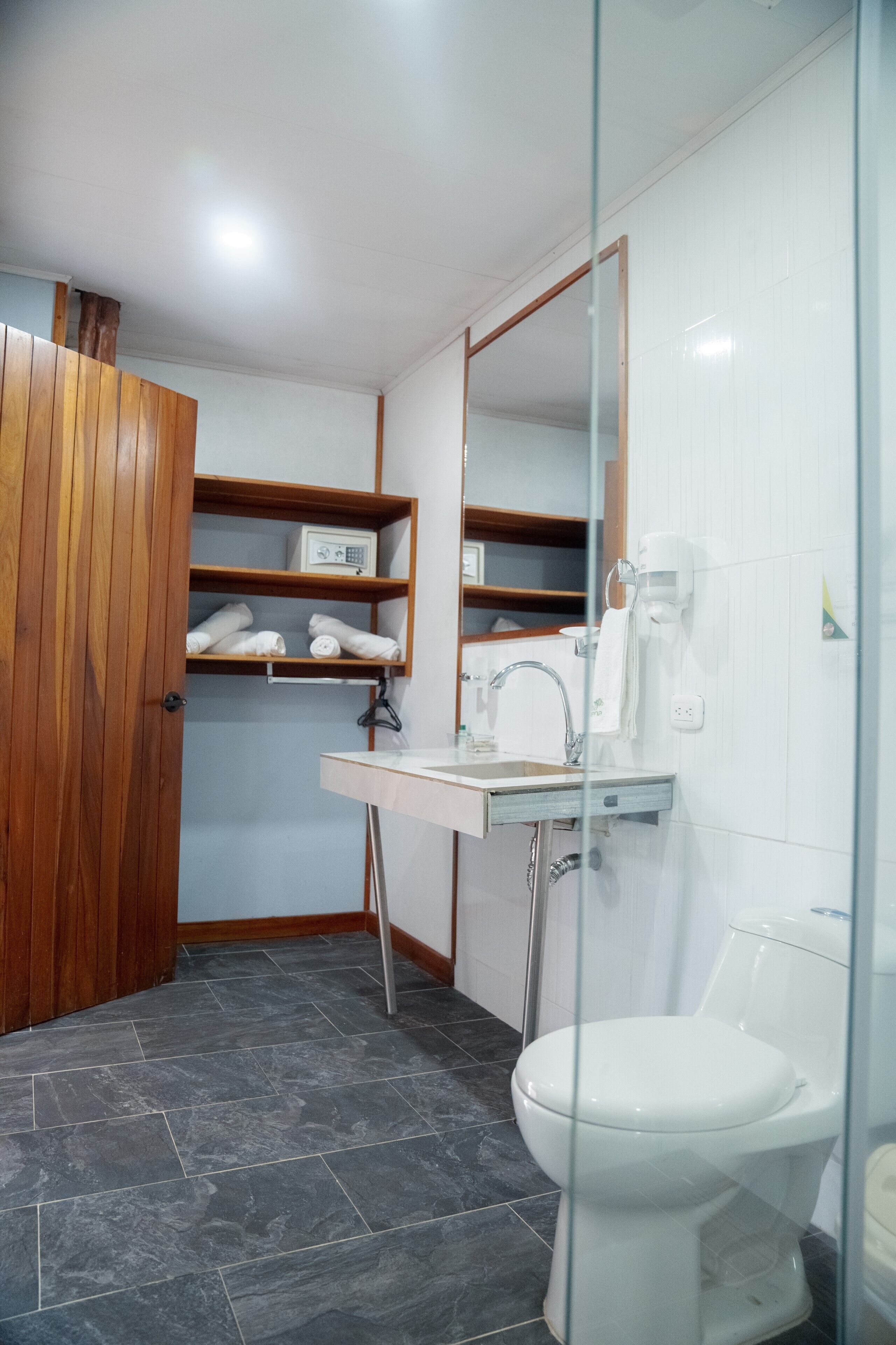 Un baño con inodoro blanco, lavabo con espejo y repisas con toallas.