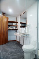 Un baño con inodoro blanco, lavabo con espejo y repisas con toallas.