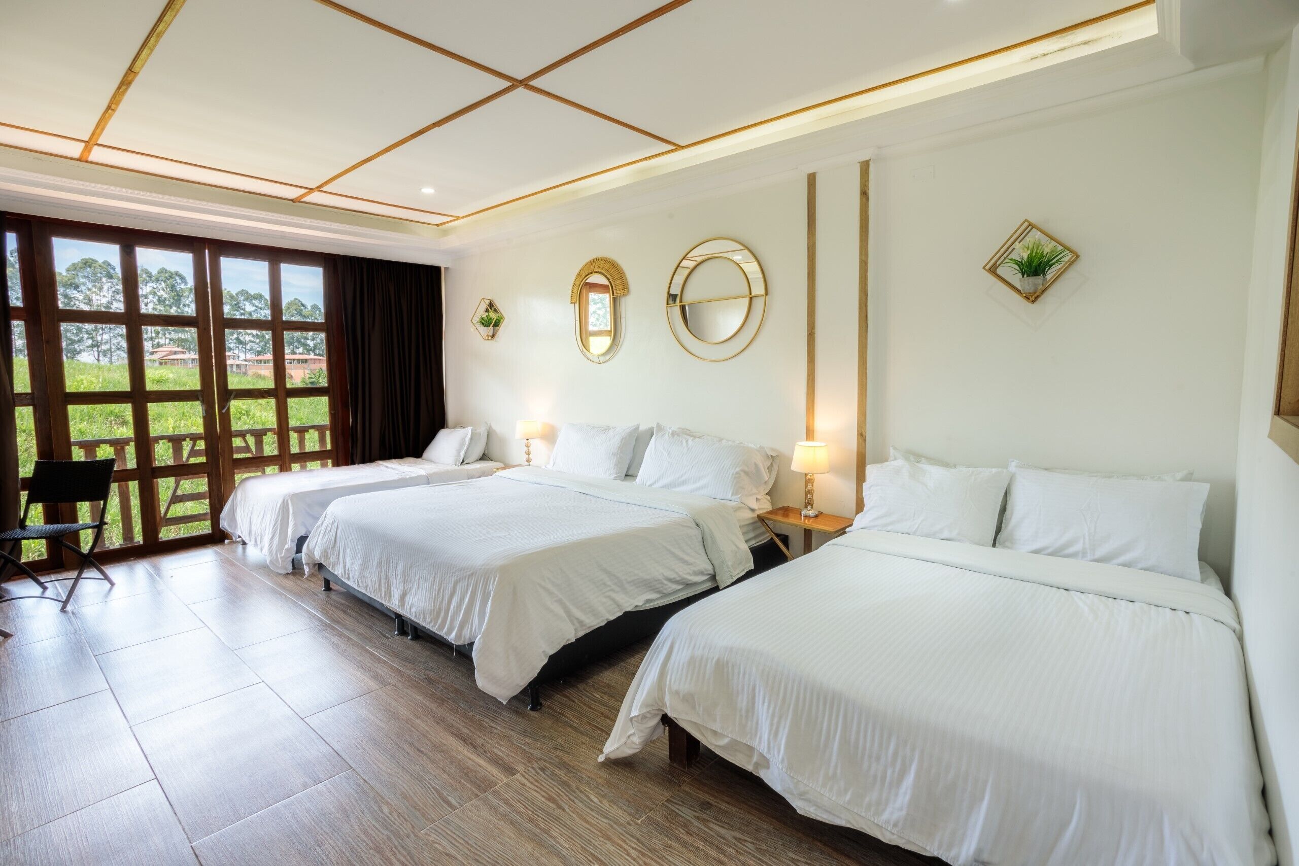 A hotel room with three beds, a large window, and a view of greenery.