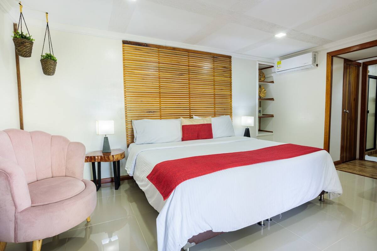 Un dormitorio con cama, una silla, una mesita de noche y un aire acondicionado de pared.