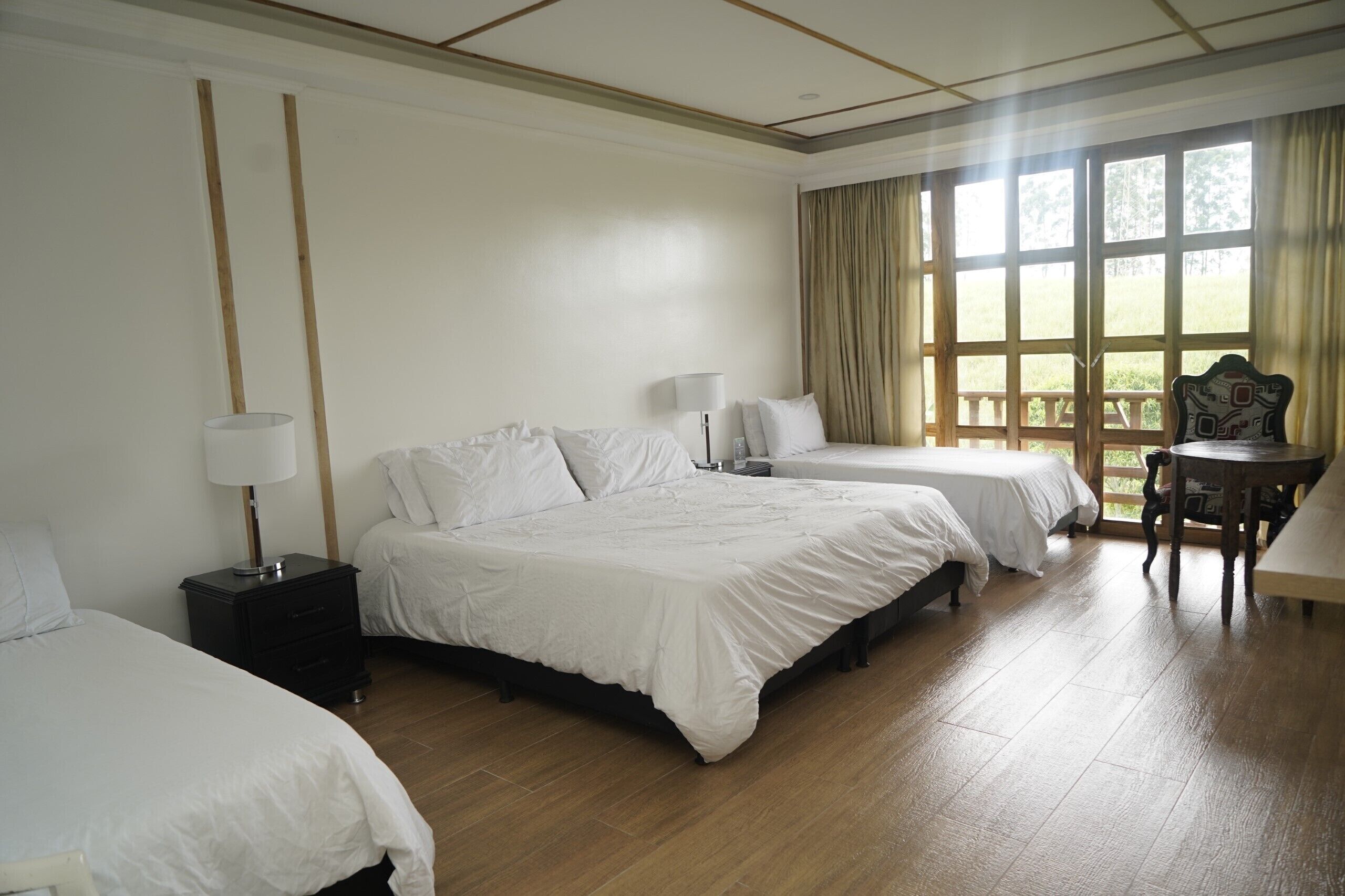 A hotel room with two beds, a small table, and a window with curtains.