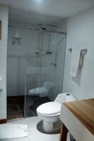 Un baño con ducha envuelta en cristal, inodoro blanco y tocador de madera.