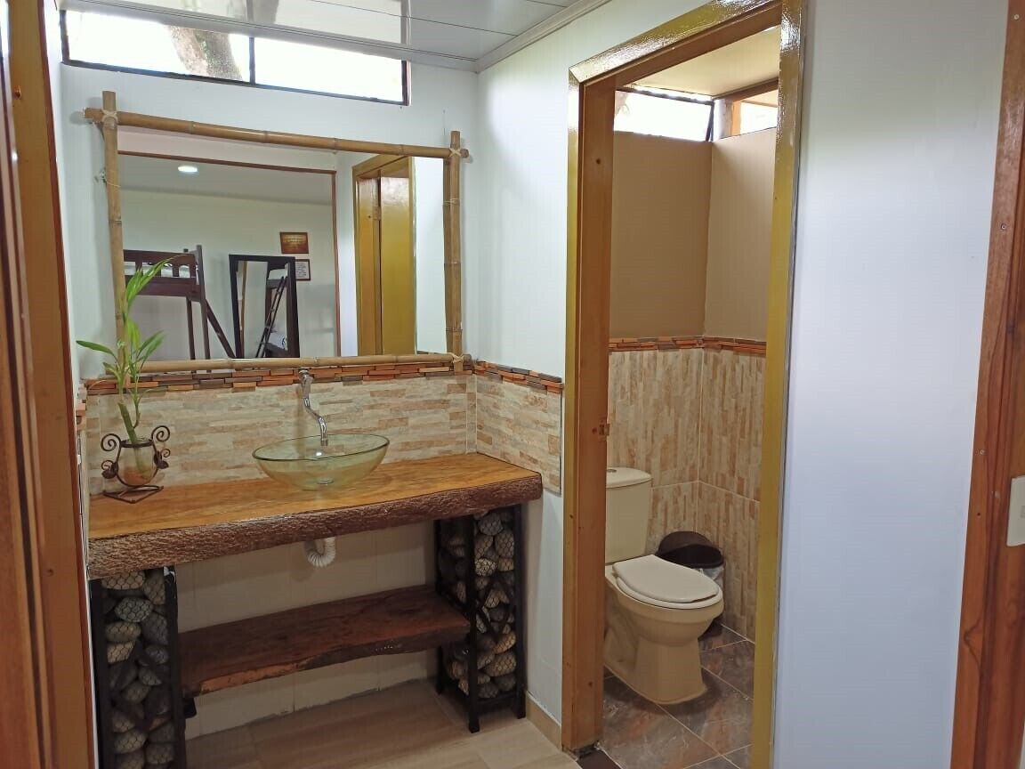 Un baño con tocador de madera, lavabo de vidrio y sanitario, además de un espejo.
