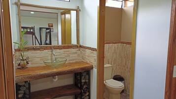 Un baño con tocador de madera, lavabo de vidrio y sanitario, además de un espejo.