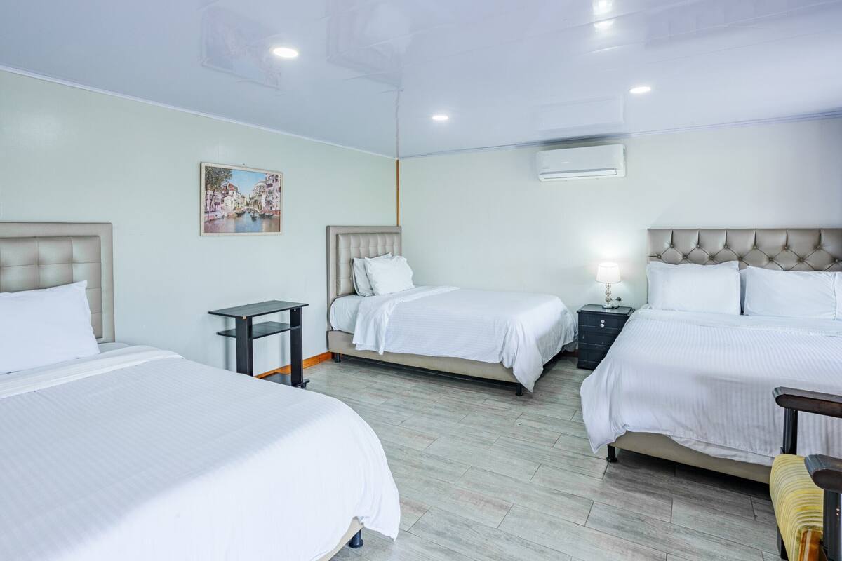 Una habitación de hotel con tres camas, un cuadro en la pared y un equipo de aire acondicionado.