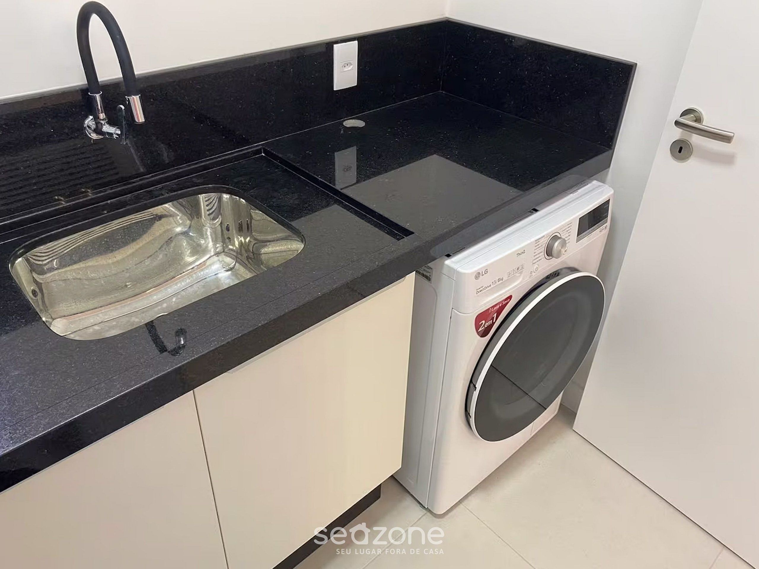A compact kitchen with a black countertop, a stainless steel sink, and a front-loading washing machine.