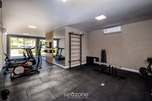 Un gimnasio con equipo de ejercicio, una banca y un estante fijado a la pared.