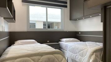 A modern hotel room with two beds, a large window, and a view of the city.