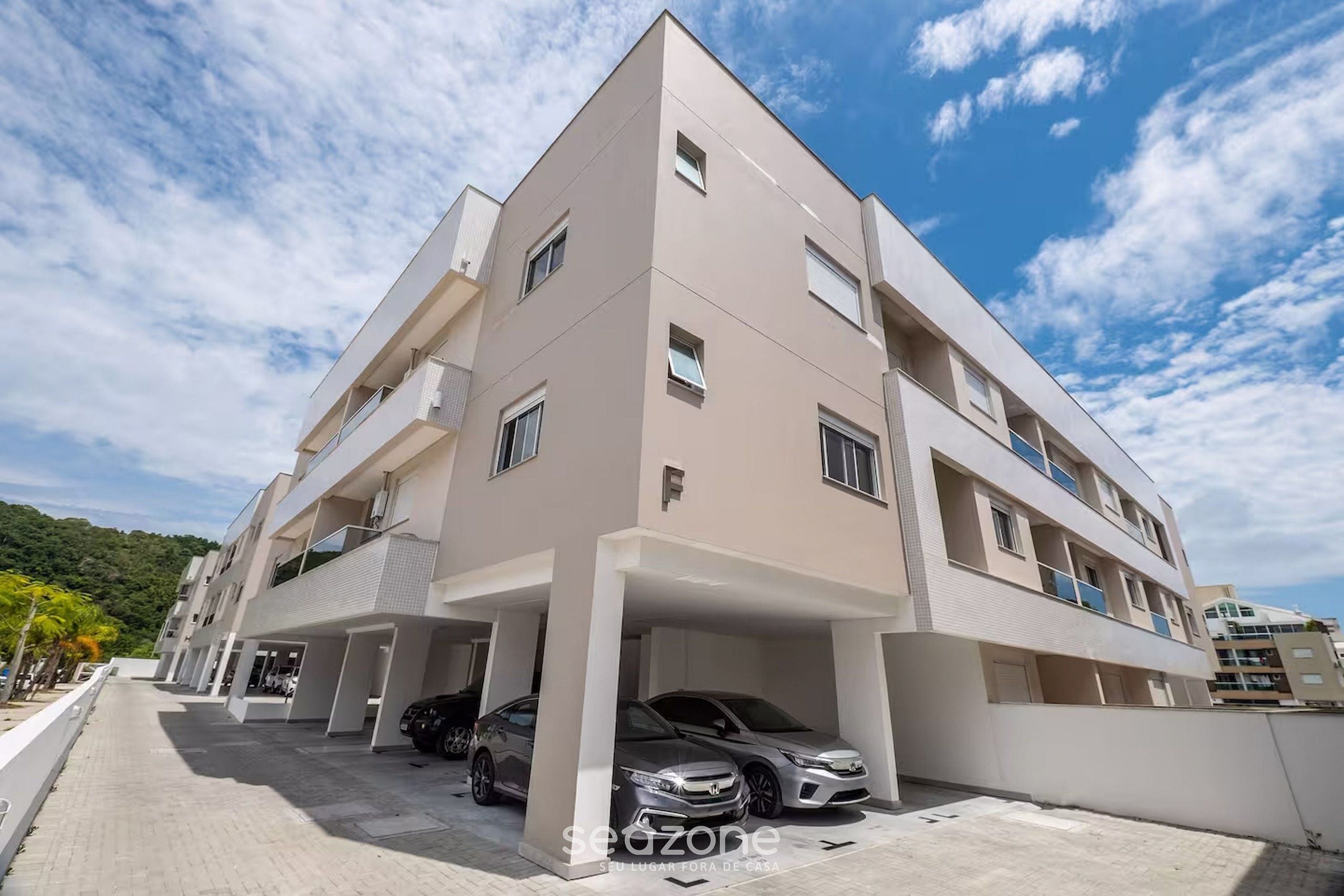 Un immeuble résidentiel à plusieurs étages, doté d’une façade plate, de balcons et d’un espace de stationnement couvert pouvant accueillir deux voitures.