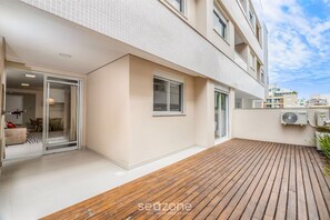 A modern apartment with a wooden deck, a sliding glass door leading to a dining area, and an air conditioning unit on the exterior wall. - Apt w/ BBQ 650 m From the Beach Ingleses Cci003 (Florianópolis)