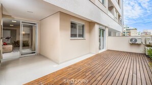 A modern apartment with a wooden deck, a sliding glass door leading to a dining area, and an air conditioning unit on the exterior wall.
