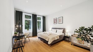 A modern bedroom with a large bed, bedside tables, a desk, and a window with curtains.